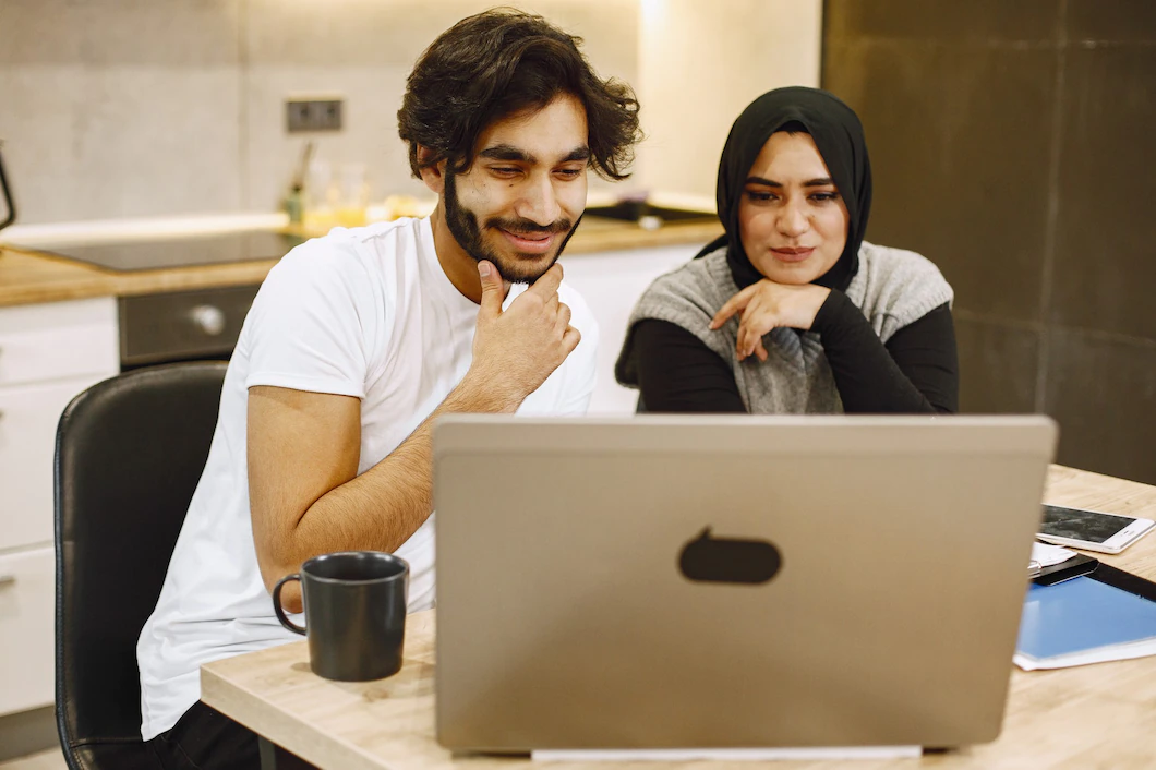 beautiful-young-couple-using-laptop-writing-notebook-sitting-kitchen-home-arab-girl-wearing-black-hidjab-1157-48423.webp